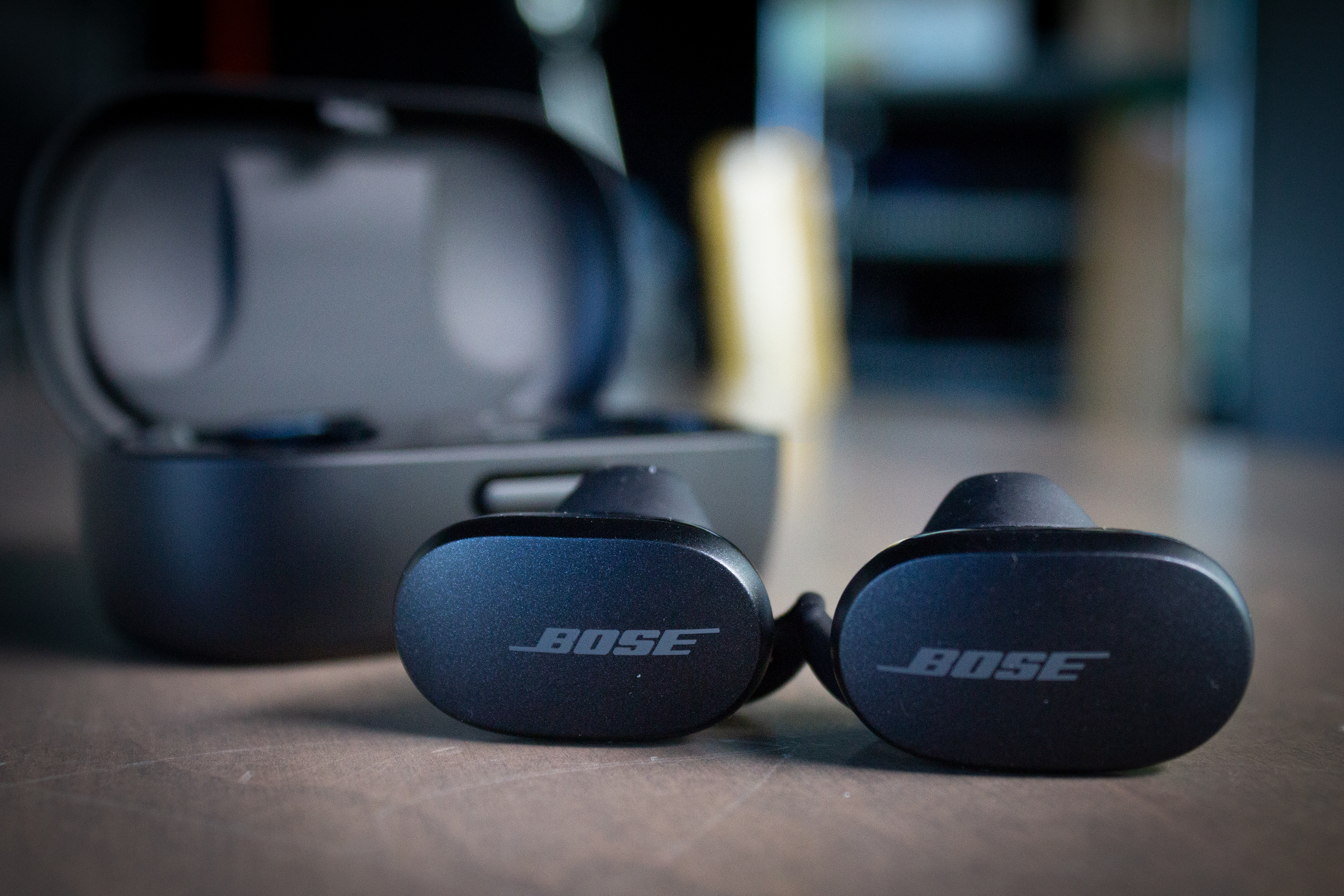 Bose earbuds on a table with logo showing and the charging case in the background